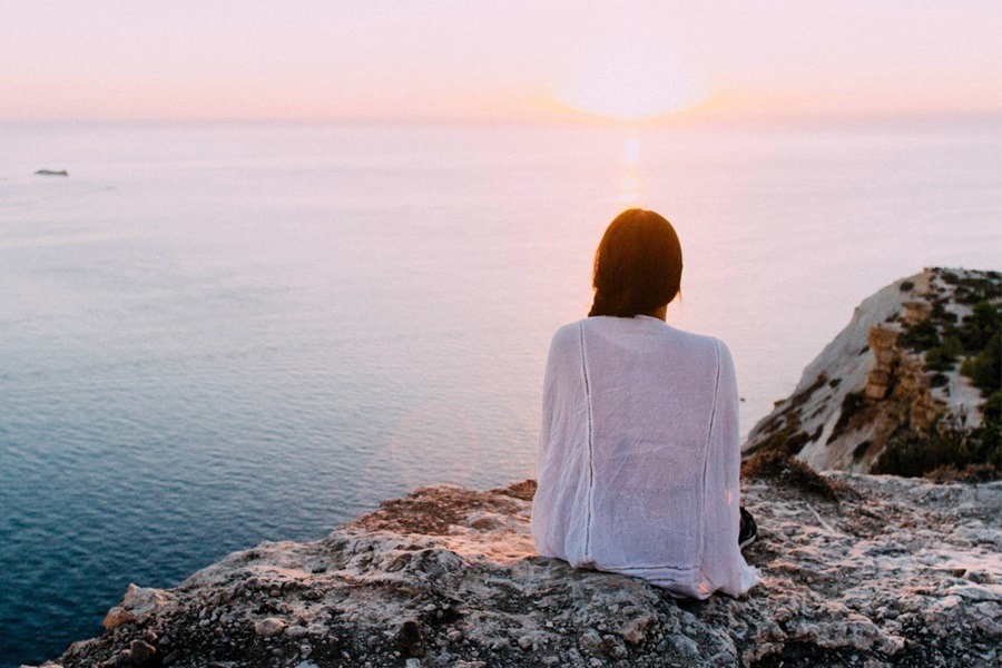 Frau sitzend auf der Klippe, Aussicht auf Wasser und Horizont, Ängste vorm Alleinreisen